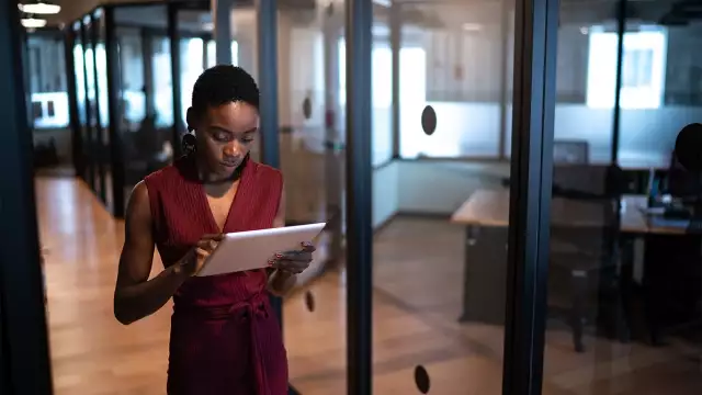 A professional woman using a tablet while walking through a modern office