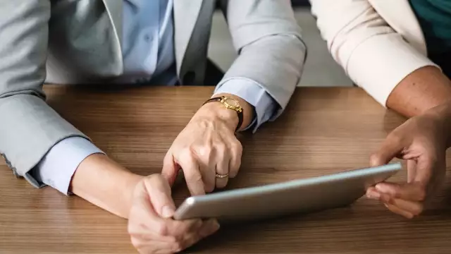 Close-up of two colleagues collaborating on a project using a digital tablet at a desk.