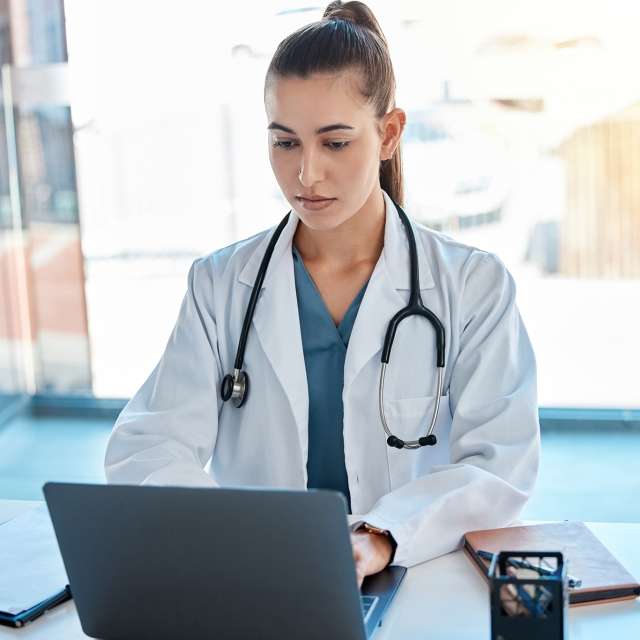 Doctor wearing stethoscope taking notes on laptop