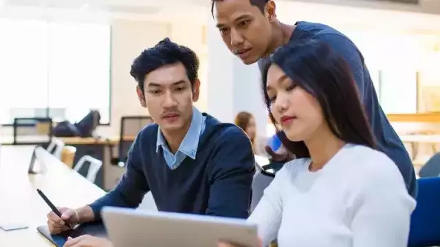 Three coworkers sitting at table around laptop