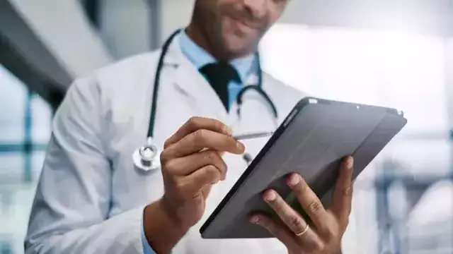 Close-up of a doctor in a lab coat using a tablet and stylus.