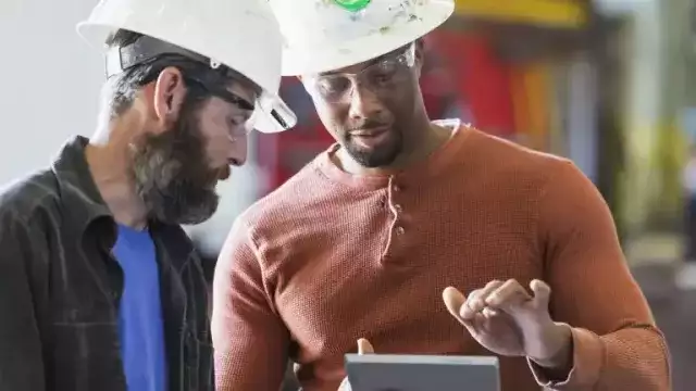 Two men wearing construction hats looking at tablet