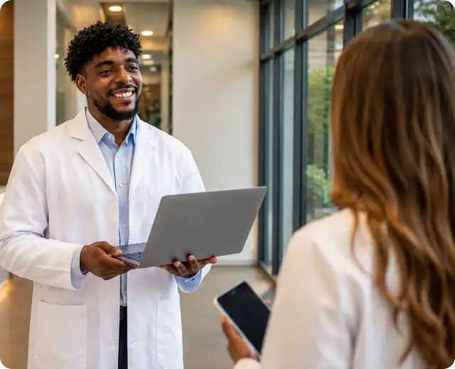 A man in a denim shirt and a female healthcare professional in a white lab coat reviewing data together on a digital tablet in an office with DNA diagrams on the wall.