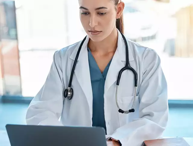 Doctor wearing stethoscope taking notes on laptop