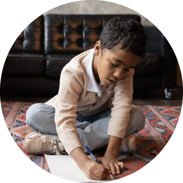 Young boy sitting on a rug and drawing on a piece of paper
