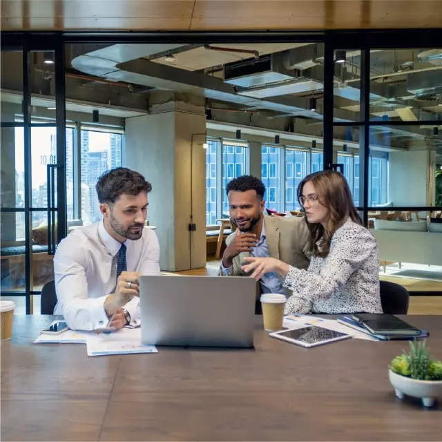 Three coworkers sitting at table around laptop