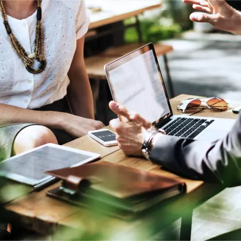 Colleagues having a discussion at a table with digital devices in an outdoor setting.