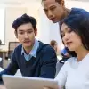 Three coworkers sitting at table around laptop