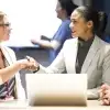 Five people stand in an auditorium while two people shake hands.